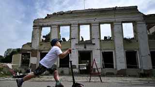 Мальчик проезжает на самокате мимо разрушенного здания мэрии в Охтырке Сумской области.
