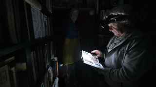 Физик Игорь Жук, 70 лет, читает книгу с помощью налобного фонарика во время отключения электричества в его доме на севере Киева