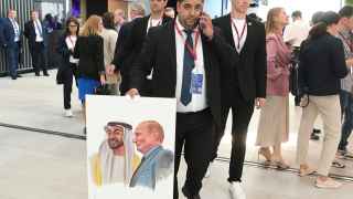 Участник ПМЭФ держит плакат с портретами Владимира Путина и президента ОАЭ шейха Мухаммеда бен Заида Аль Нахайяна.