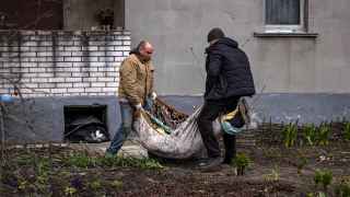 Коммунальщики несут в ковре тело мужчины, похороненного в своем дворе в Гостомеле Киевской области.